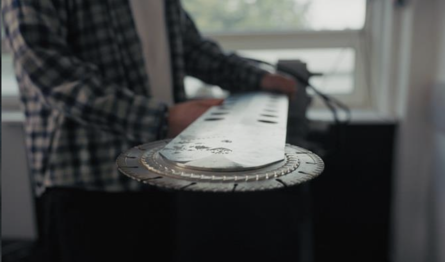 A team member holding the prototype arm and diamond blade by the workshop window