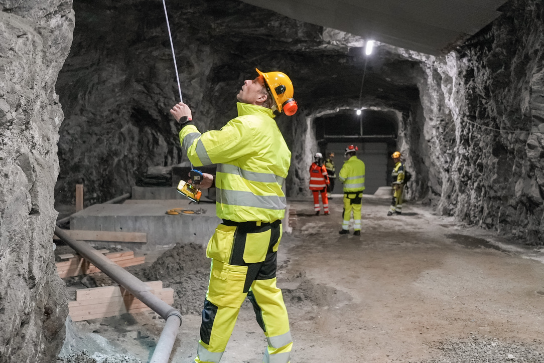 Personer med hjelm og refleksklær som inspiserer fjellveggene i en tunnel