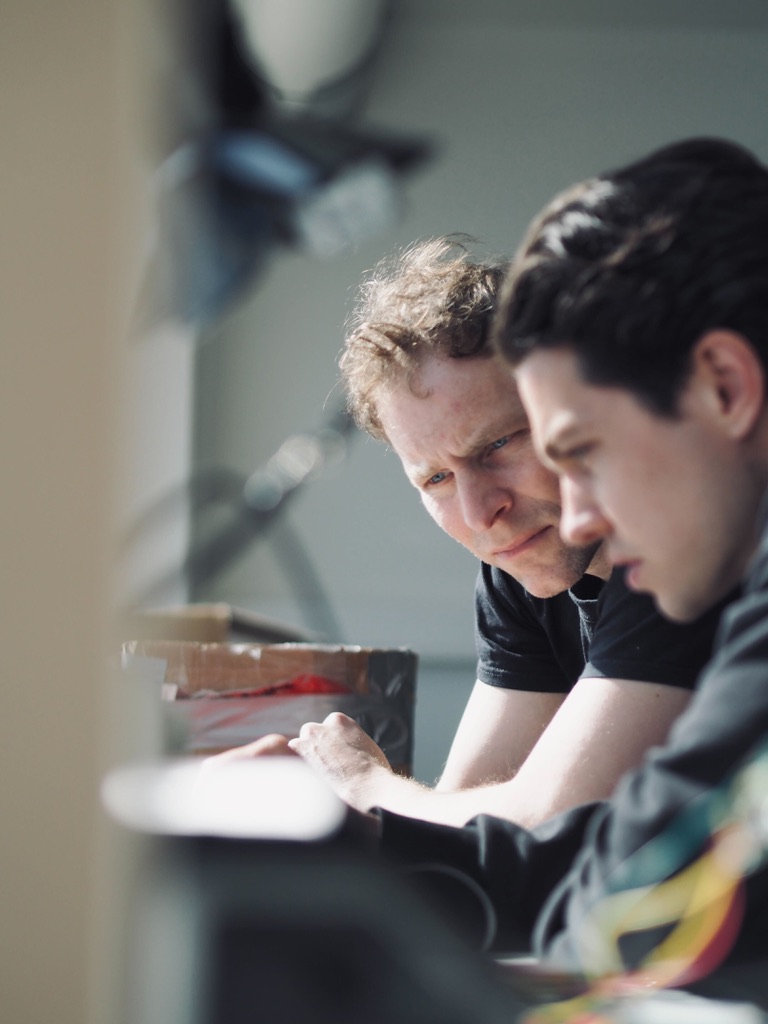 Two team members looking closely at work on a bench