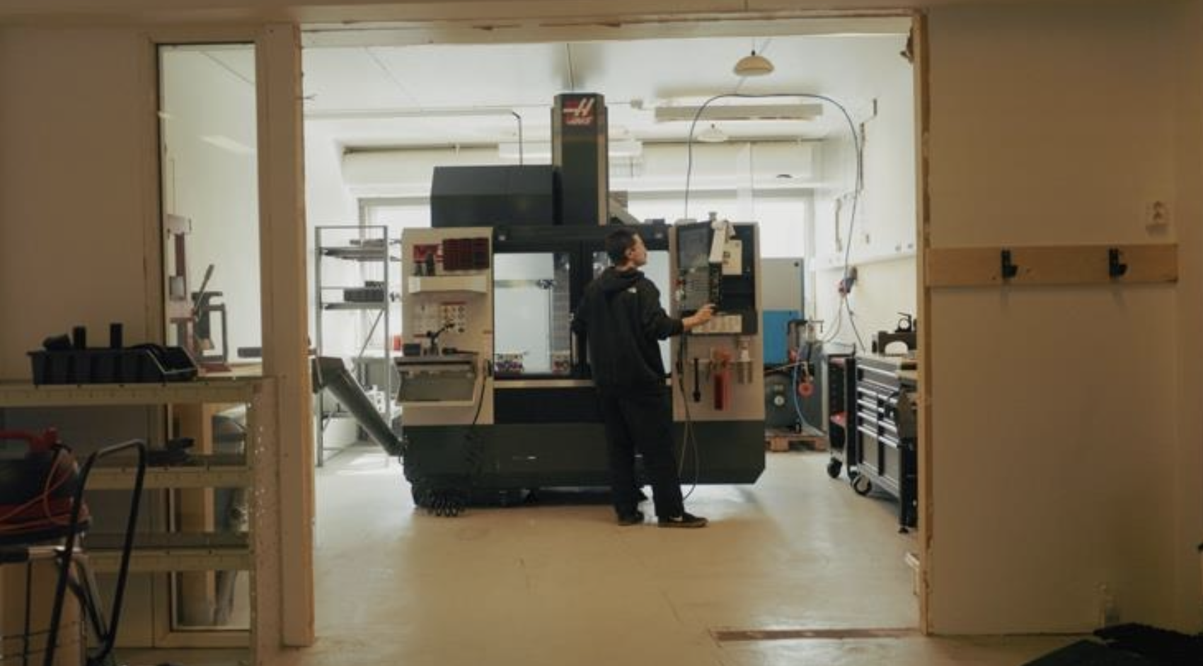 Seen through a doorway: a team member at the CNC machine in the workshop